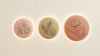 illustration of three softly glowing circular forms arranged in a gentle progression from left to right, each slightly larger than the last, rendered in warm blush, dusty gold, and soft terracotta tones against a cream background. 